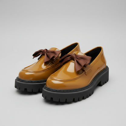 Pair of mustard yellow shoes with brown bows on a textured surface