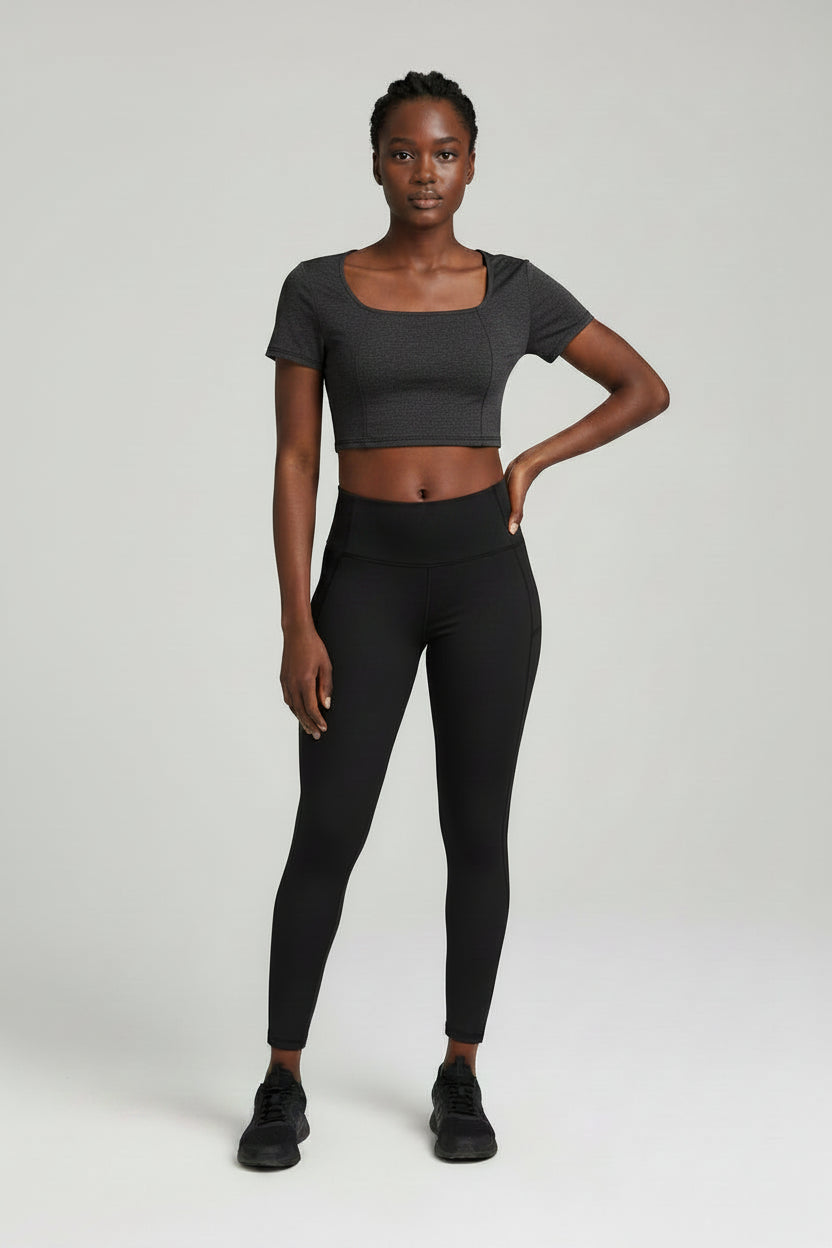 Woman wearing a gray crop top and black leggings on a white background