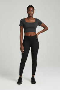 Woman wearing a gray crop top and black leggings on a white background