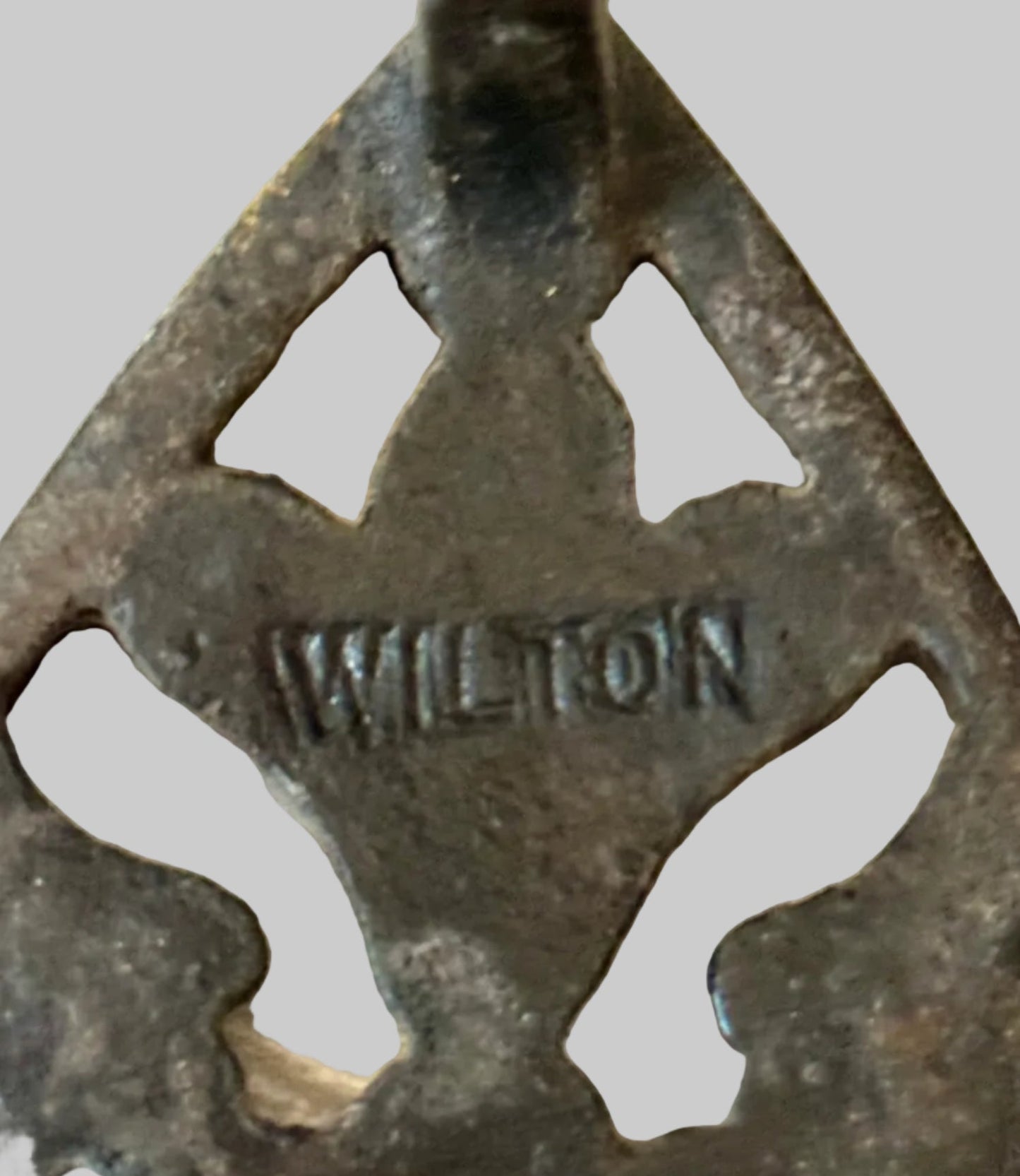 Vintage metal trivet with 'Wilton' branding on a wooden surface