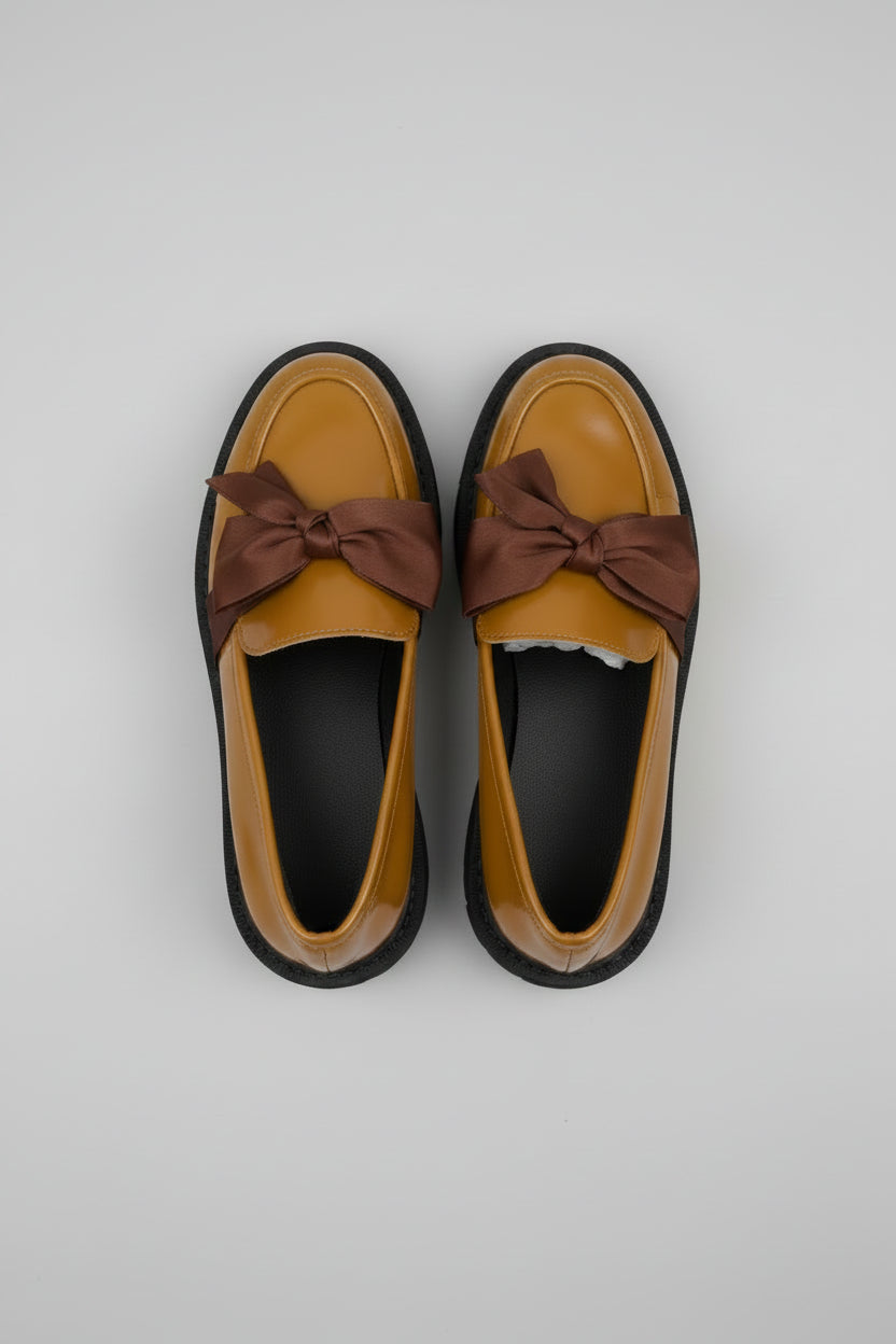 Pair of mustard yellow shoes with brown bows on a gray fabric background
