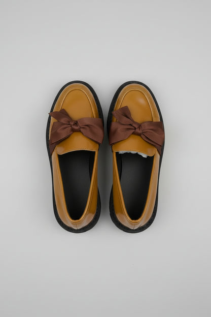 Pair of mustard yellow shoes with brown bows on a gray fabric background