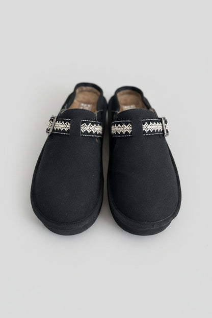 Pair of black slippers with decorative bands on a textured surface