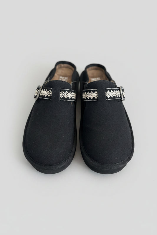 Pair of black slippers with decorative bands on a textured surface