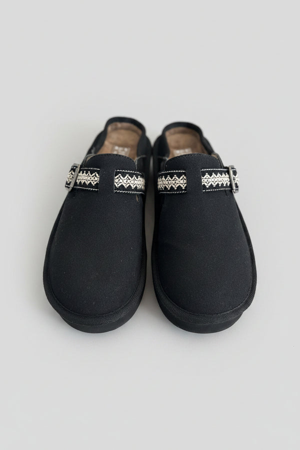 Pair of black slippers with decorative bands on a textured surface