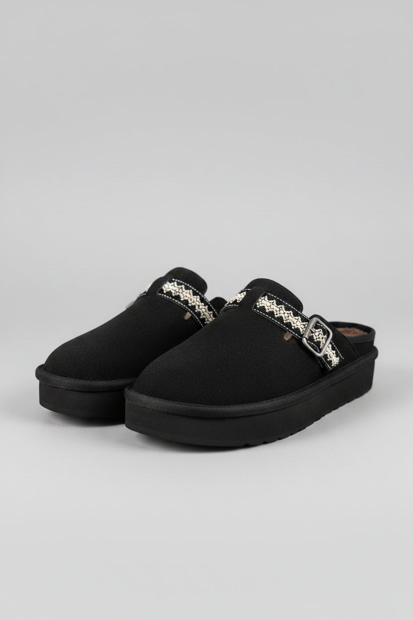 Black slippers with decorative buckles on a textured surface