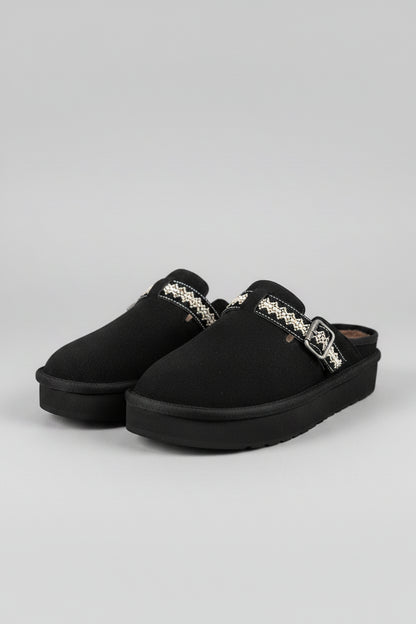 Black slippers with decorative buckles on a textured surface