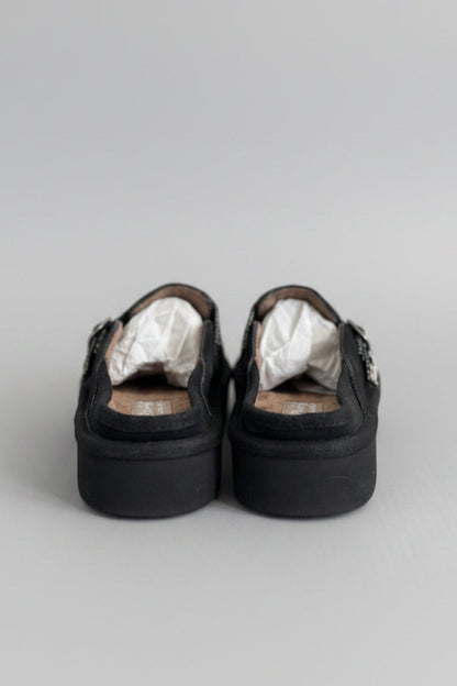 Pair of black platform shoes with white lining on a beige surface, blurred indoor background
