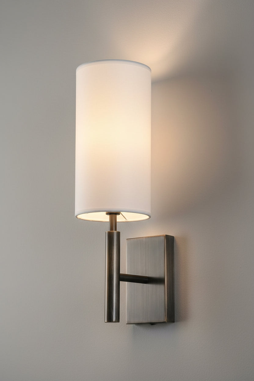 Wall-mounted light fixture with a white shade and metallic base on a white background
